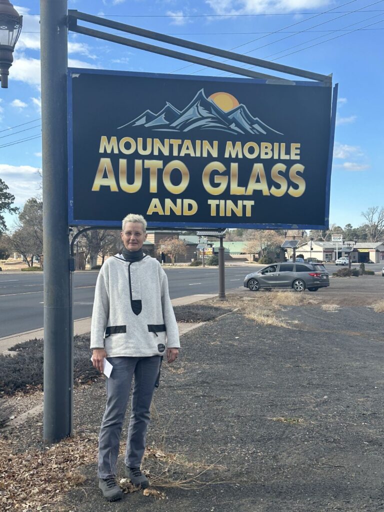 Lady in white sweater with $500 check by the Mountain Mobile Auto Glass And Tint sign.